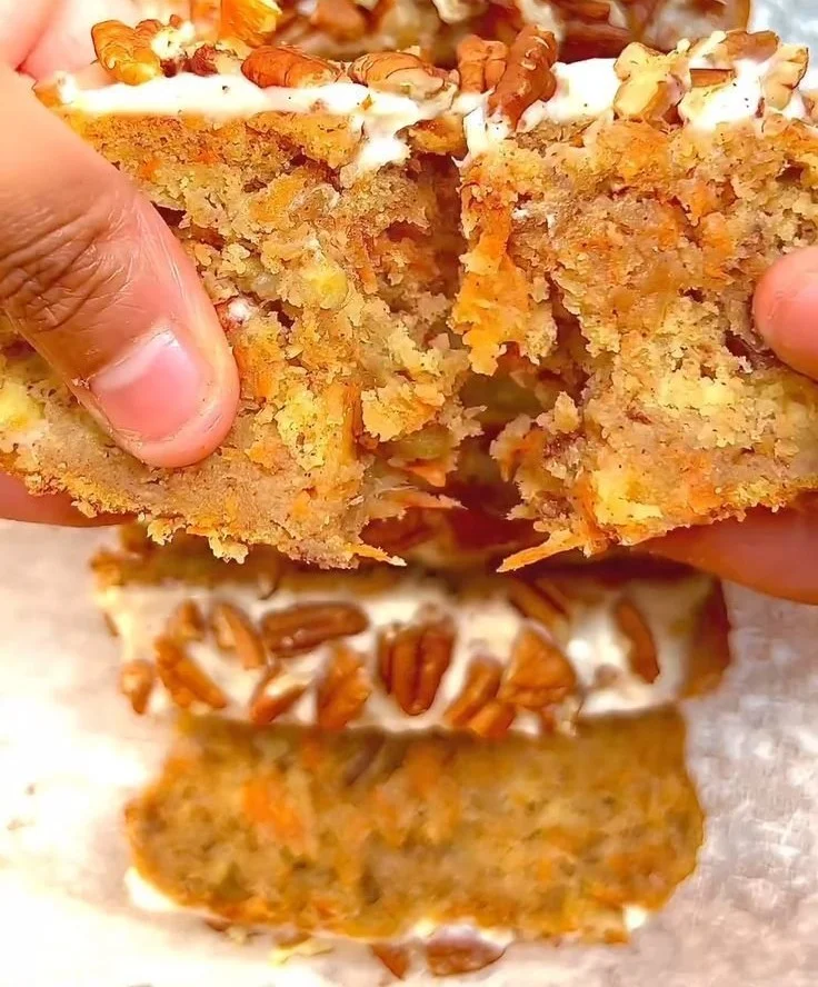 Delicious carrot cake banana bread sliced on a wooden board with cream cheese frosting.